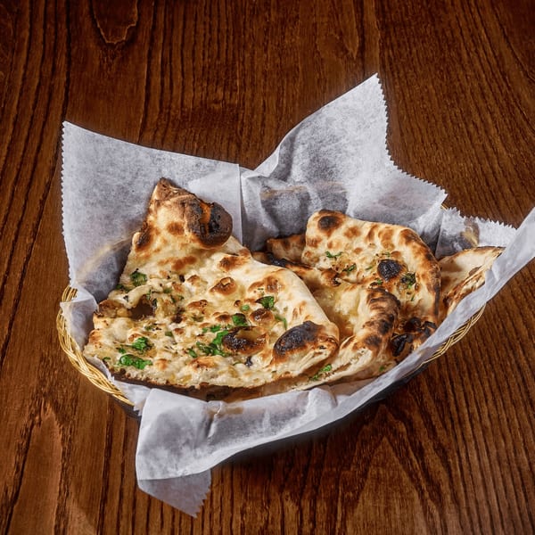 Golden brown naan bread with cilantro and garlic in a basket on a wooden table.