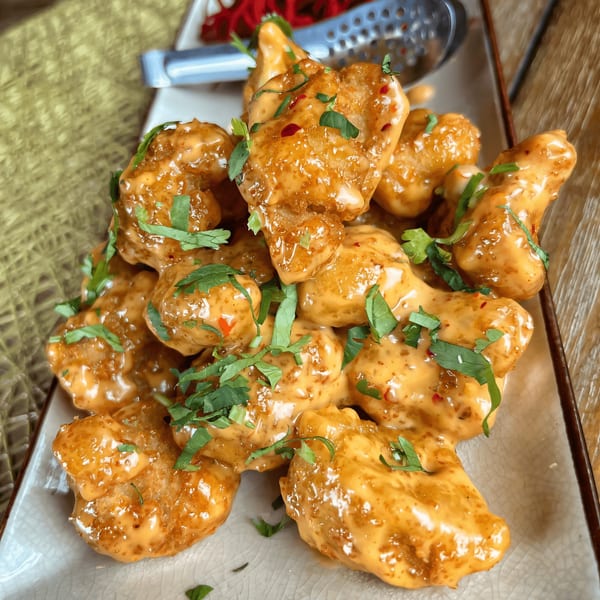 A plate of crispy shrimp coated in a creamy orange sauce, garnished with fresh green herbs.