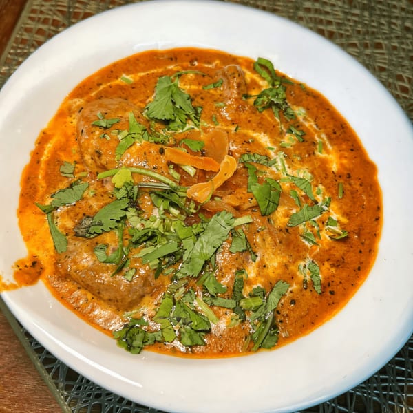 Indian butter chicken in a white bowl, garnished with fresh cilantro and cream swirls.