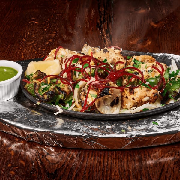 Sizzling chicken tikka with red onions, green peppers, and lemon on a dark wooden table.