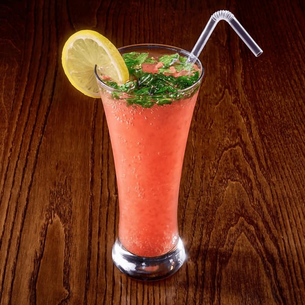 Pink drink with mint leaves, a lemon slice, and a straw in a tall glass on a wooden table.